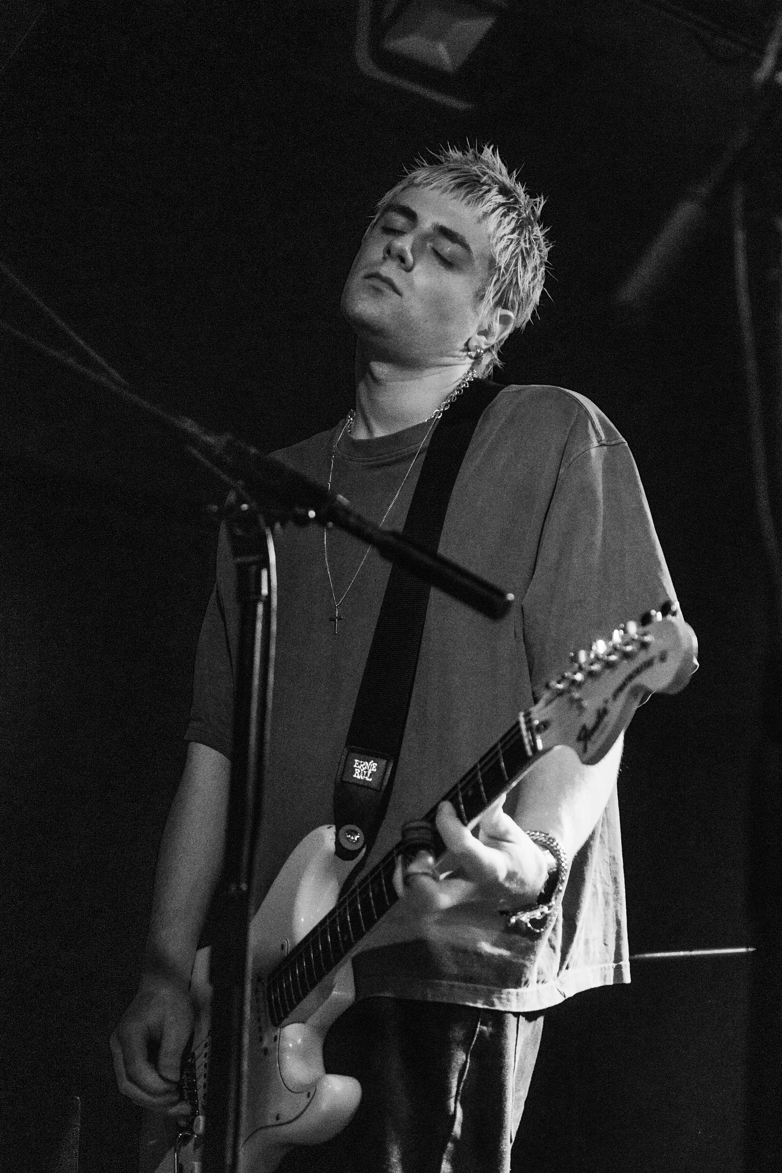 Black-and-white photograph of a Bleech 9:3 guitarist playing beside a microphone stand at The Grace in London in 2025