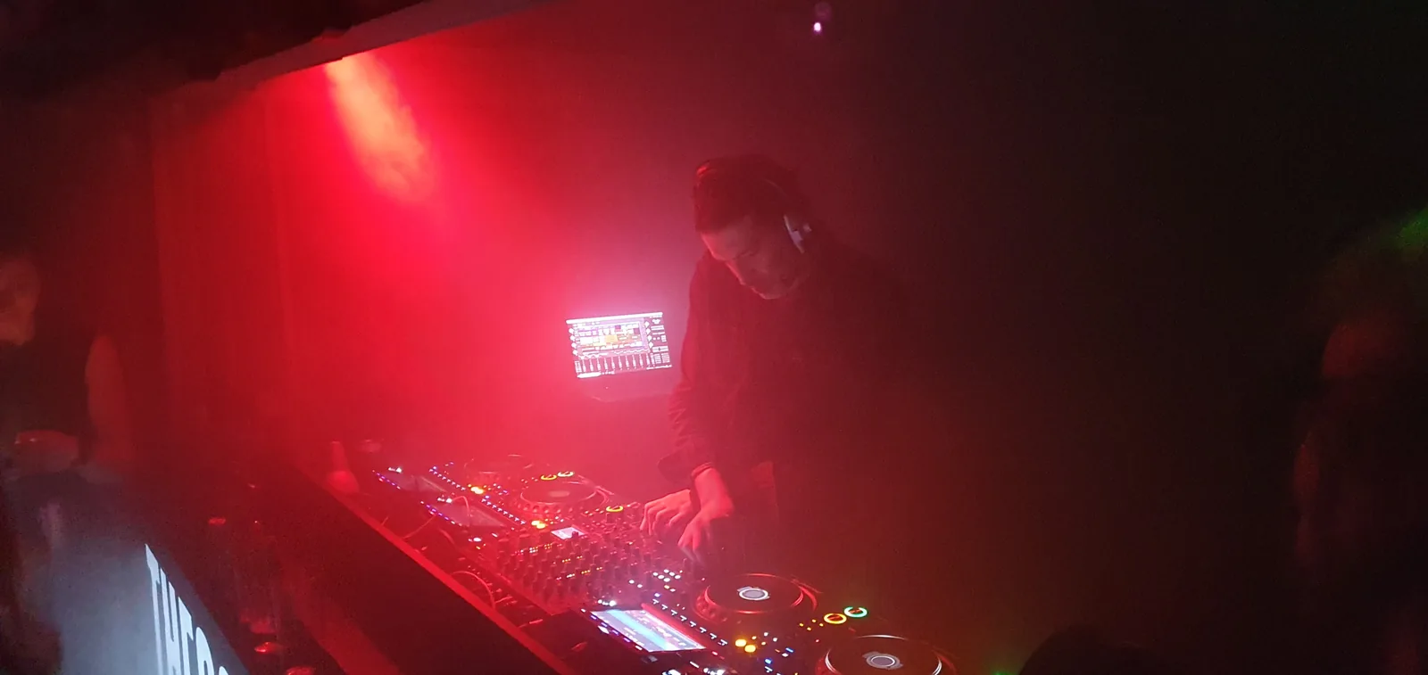 Erol Alkan wearing headphones and working at DJ decks under red light at The Social in London