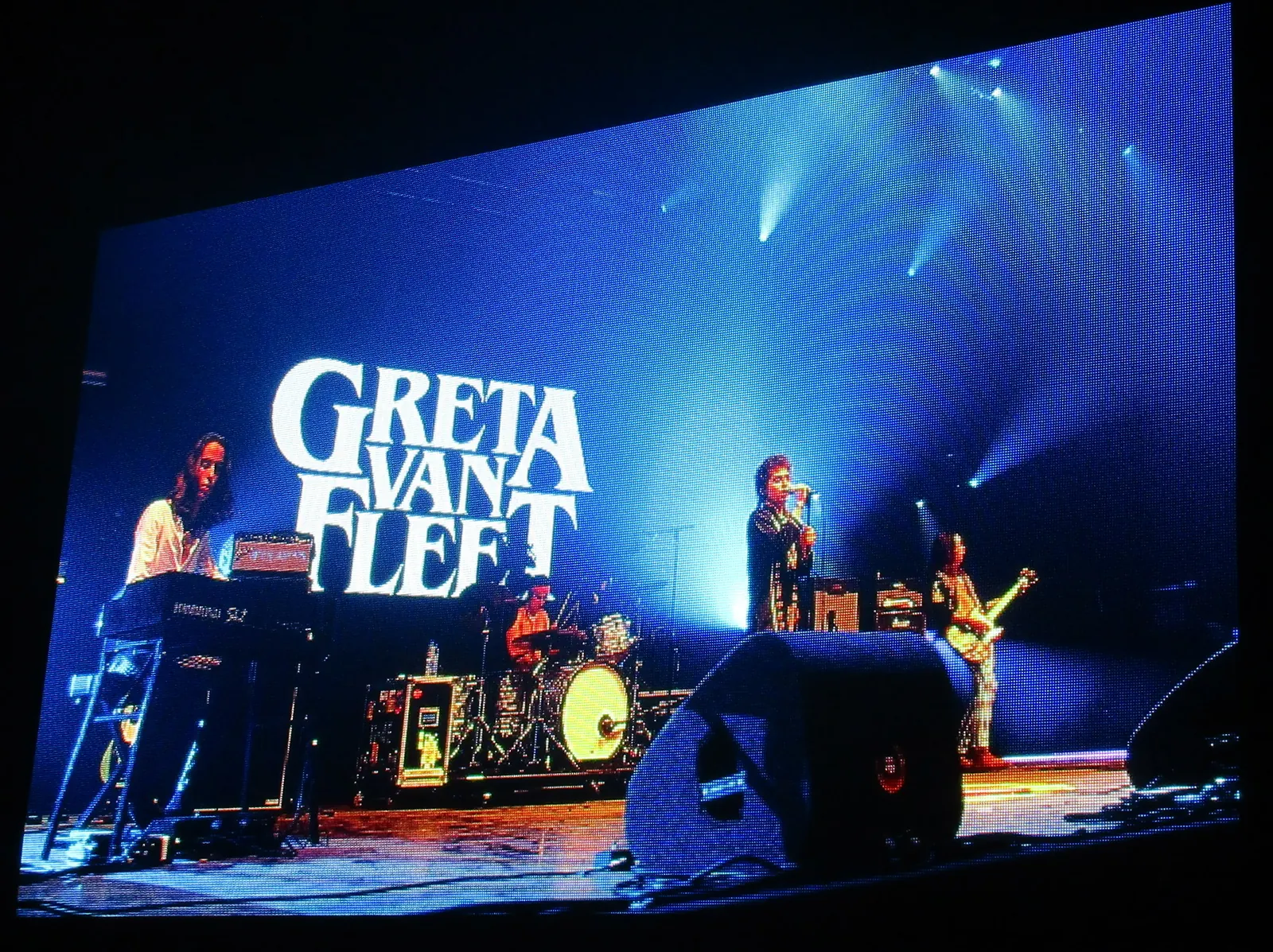 Greta Van Fleet’s singer and instrumentalists displayed on a blue-lit festival screen with the band’s name at Pinkpop in 2018