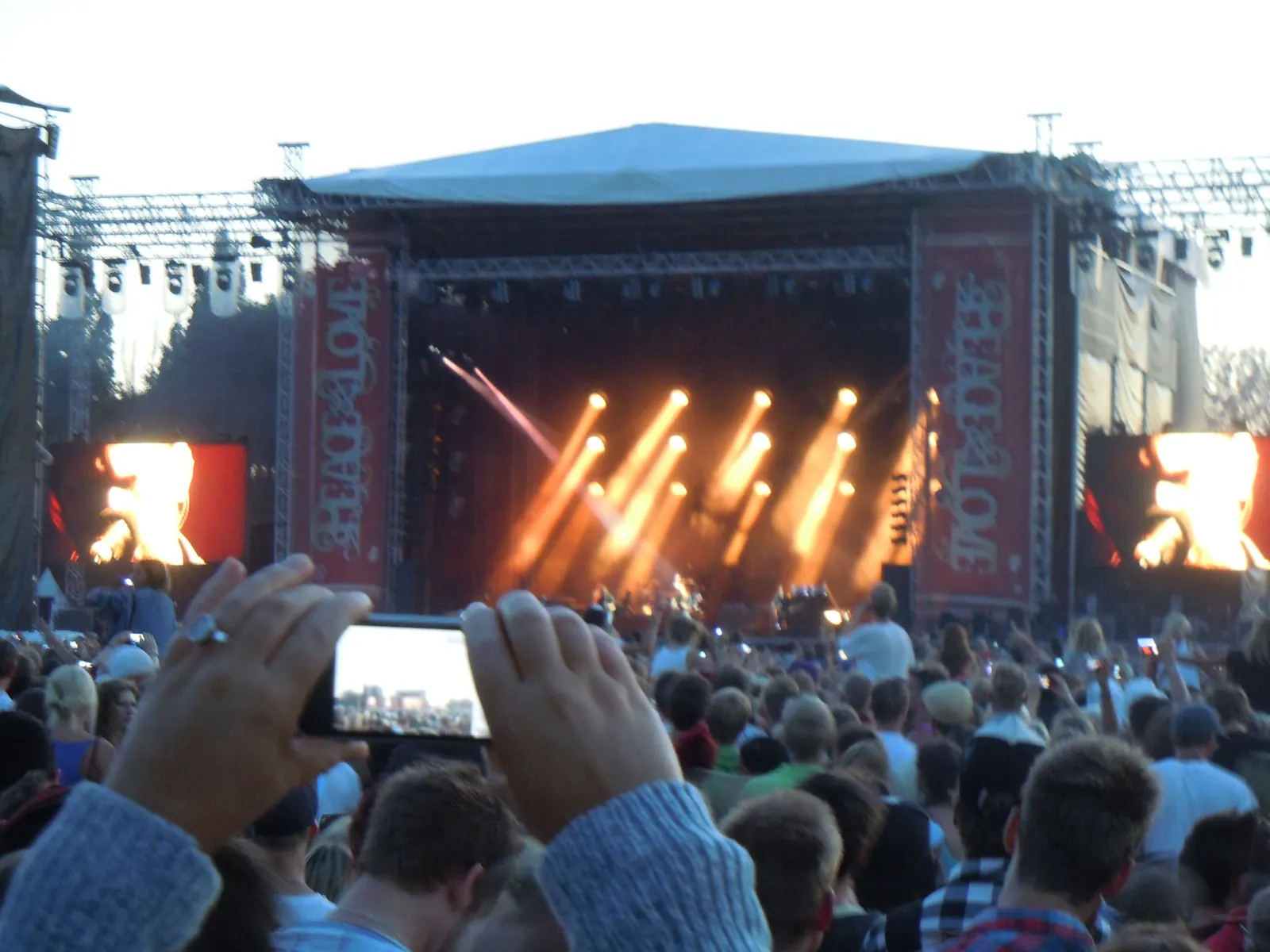 Crowd facing a festival stage with orange spotlights and large video screens during Kings of Leon’s 2011 Peace & Love performance