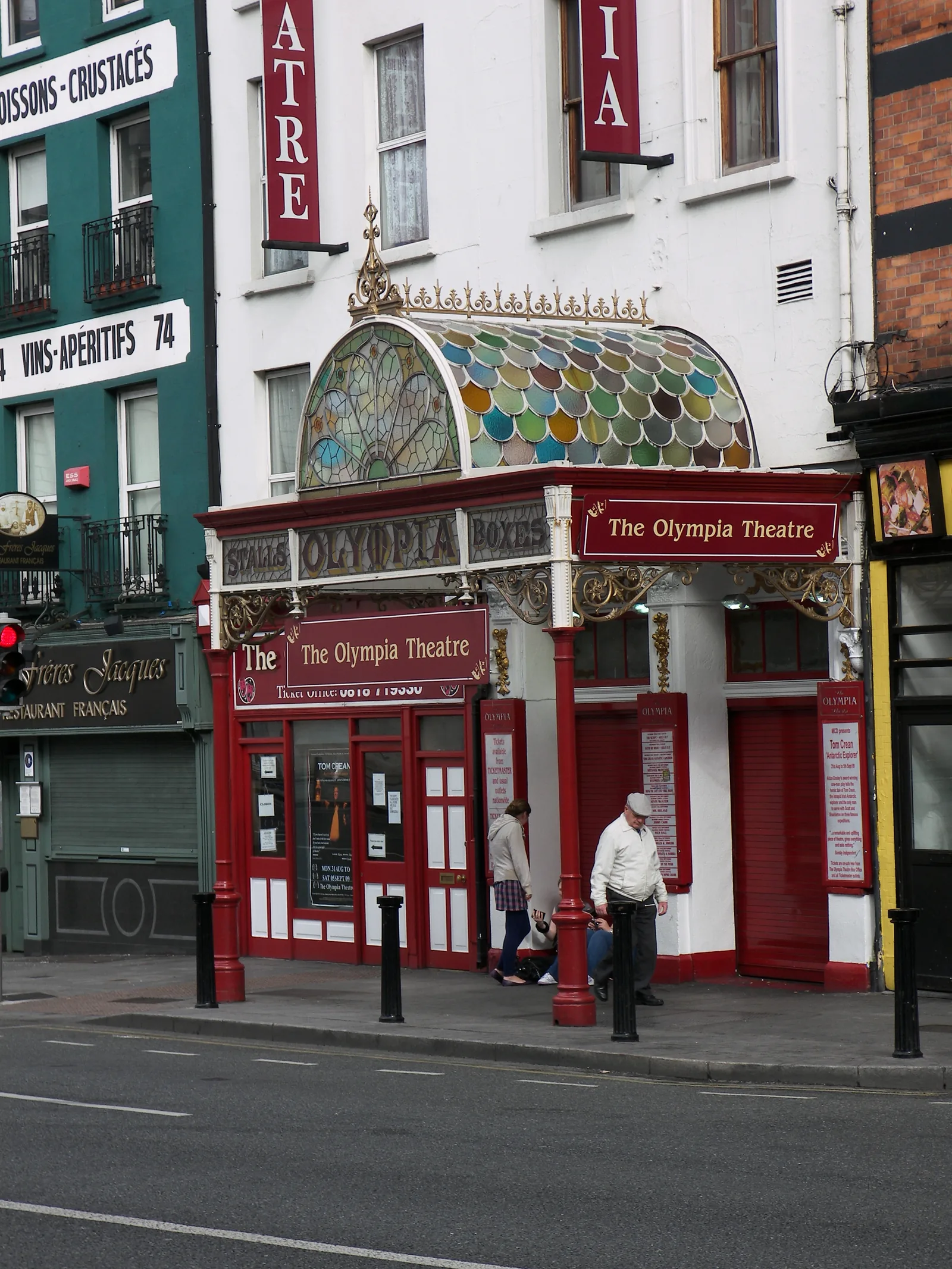 Red entrance and multicoloured glass canopy of Dublin’s Olympia Theatre, with pedestrians on the pavement