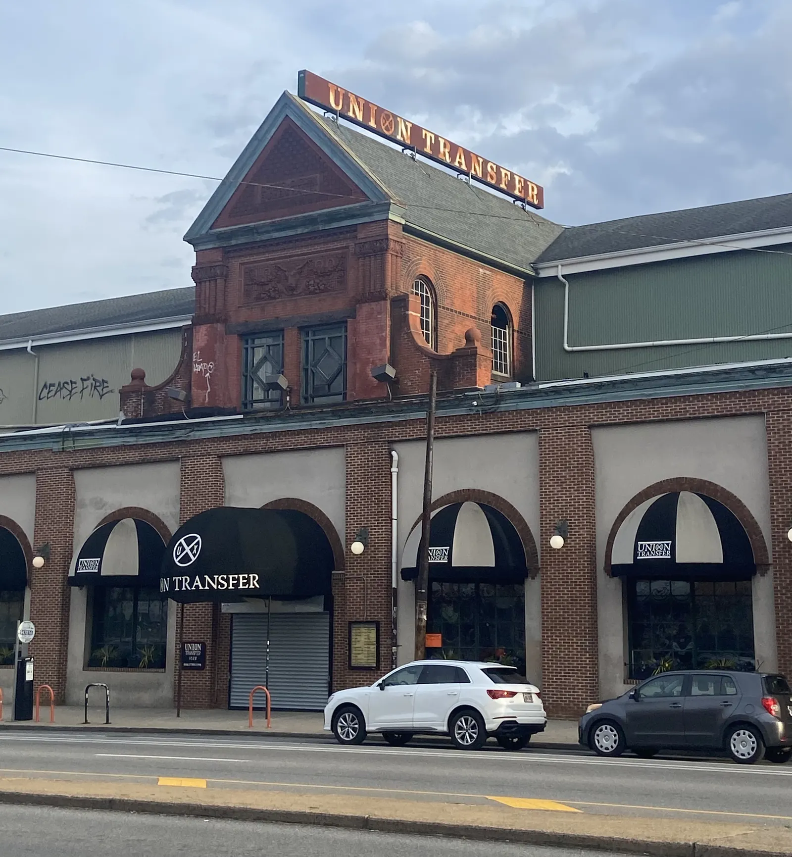 Brick Union Transfer music venue with a rooftop sign, black window awnings and cars along the street