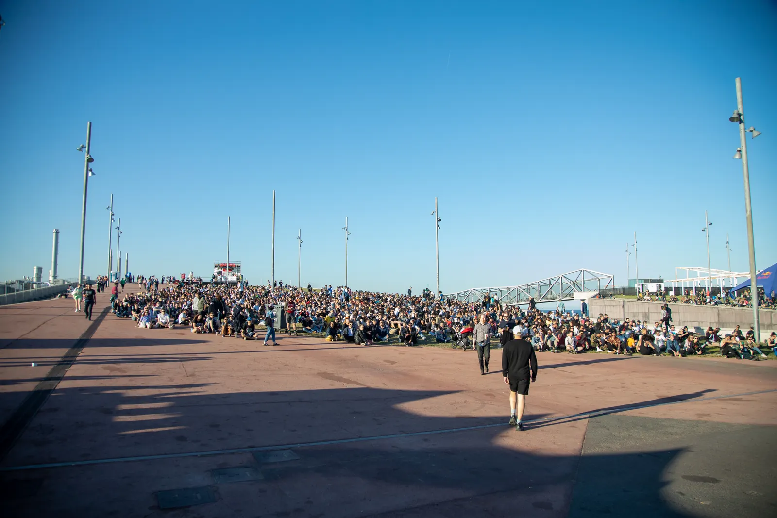 A festival crowd seated and standing on a sloping outdoor area beneath a clear blue sky at Primavera Sound in 2019