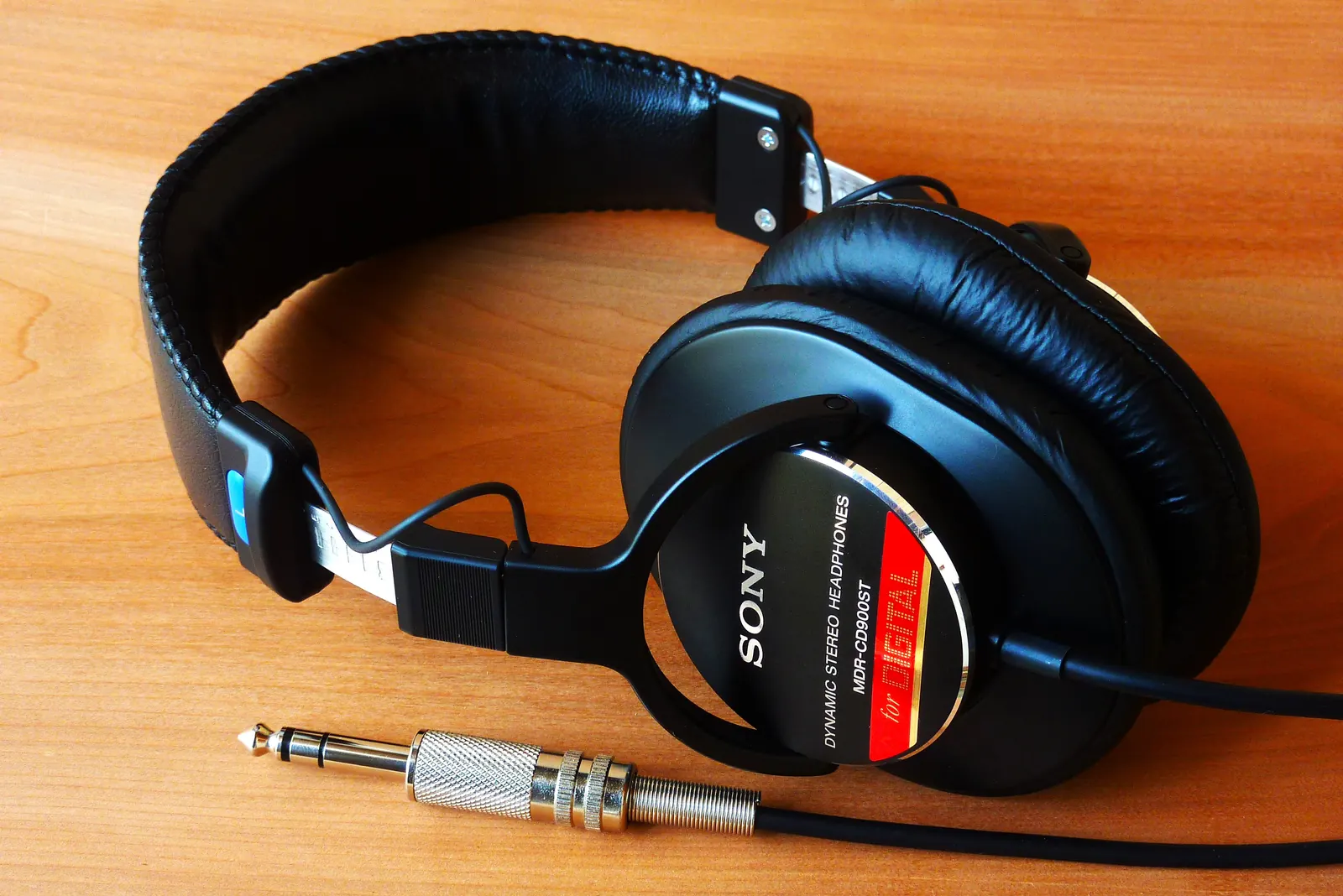 Black Sony over-ear headphones and a silver audio plug on an orange wooden surface