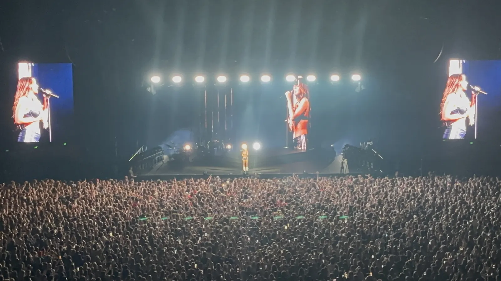 Tate McRae performing on an arena stage with large video screens and an audience in Adelaide in 2024