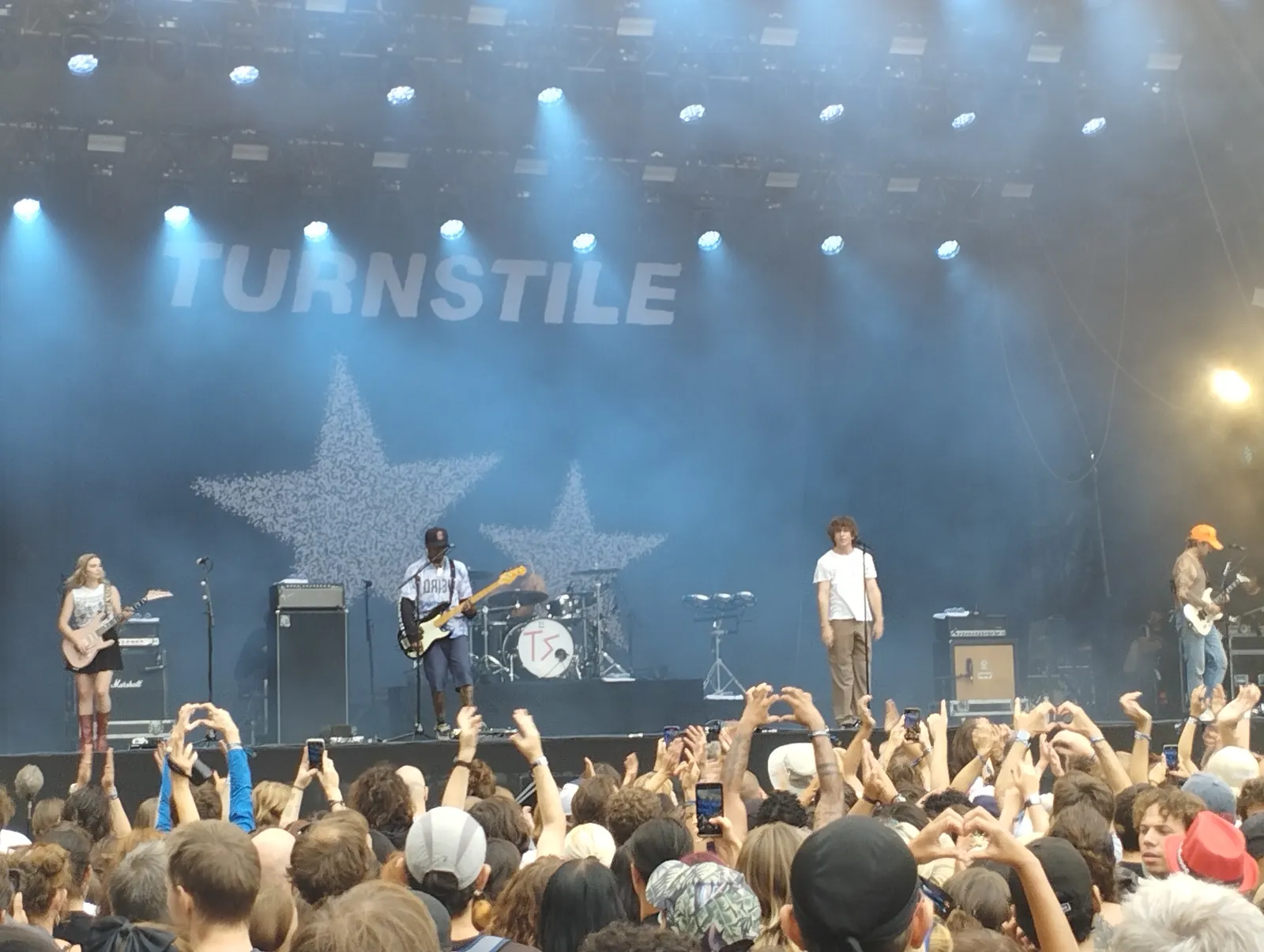 Turnstile musicians onstage beneath blue lights and a large band-name backdrop, with raised hands and phones in the crowd at Rock en Seine in 2023