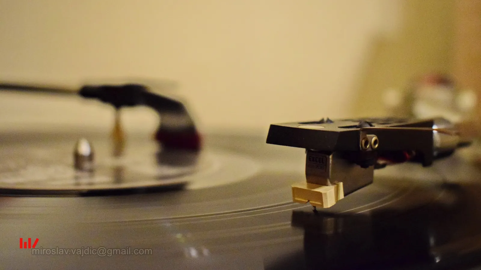 A turntable cartridge over a black vinyl record beside a record-cleaning brush