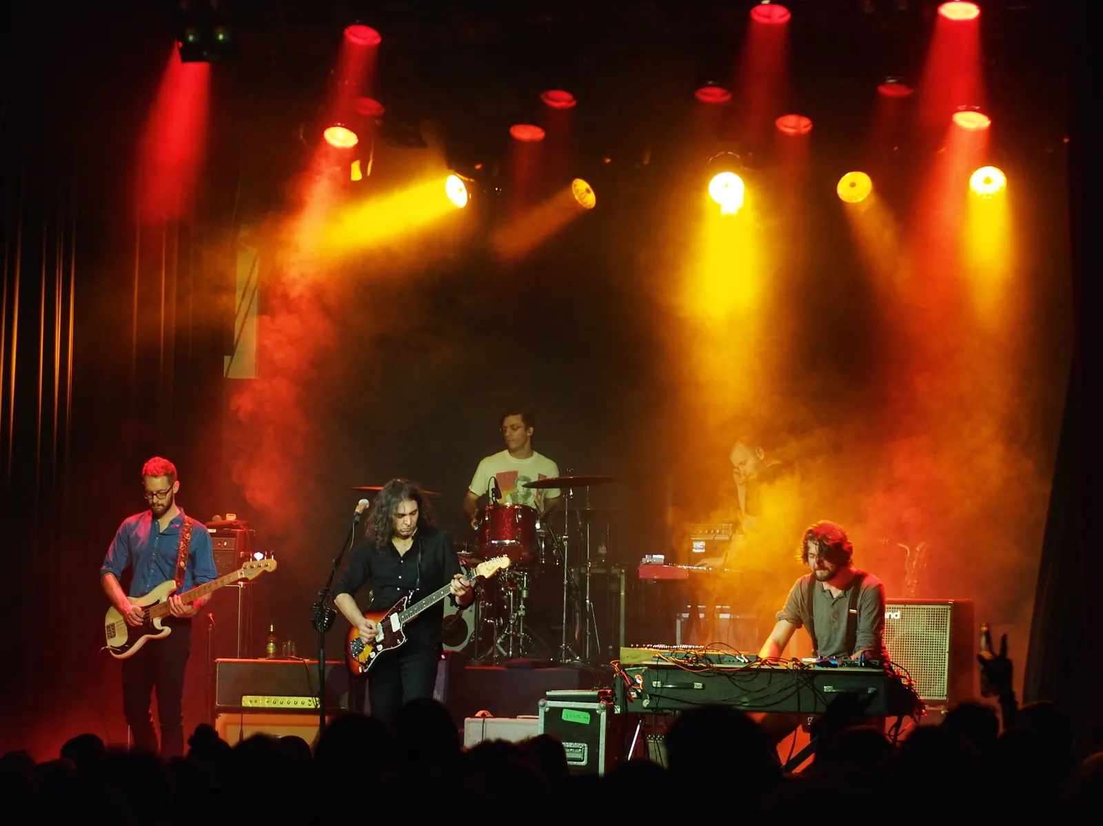 The War on Drugs performing under red and yellow stage lights, with guitars, drums and keyboards